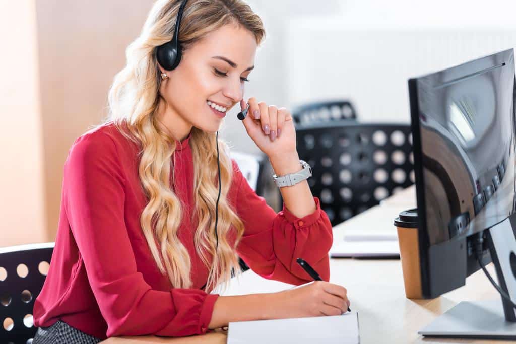 A female employee taking a customer call while writing notes.